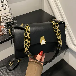 Close-up detail of a chic black leather square bag featuring a gold chain strap and metal clasp