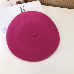 Close-up view of a vibrant magenta wool beret hat placed on a white table surface