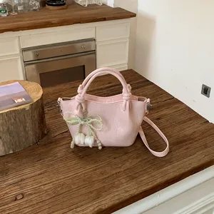 Detailed view of a pink faux leather bucket bag with pearl bow charm on a wooden counter