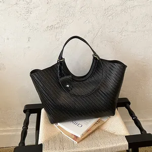 Close-up detail of a large black woven tote bag featuring a minimalist handle design