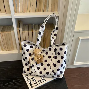 Detailed view of a white polka dot canvas tote bag with a cute teddy bear charm on it