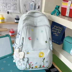 Zaino scolastico azzurro con ricami floreali e ciondolo in peluche in un ambiente di studio