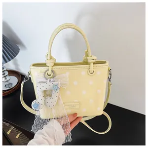 Detailed view of a yellow polka dot handbag featuring a lace bow and note charm