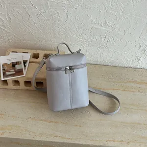 Dettaglio di una borsa a tracolla cilindrica grigio chiaro minimalista con doppia zip.