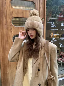 Aziatisch model draagt een gezellige beige gebreide muts met oorbescherming en pompon