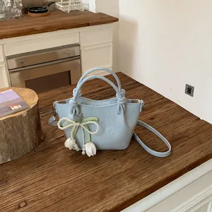 Detail of light blue bucket bag with a pearl bow tulip charm on a rustic wooden table