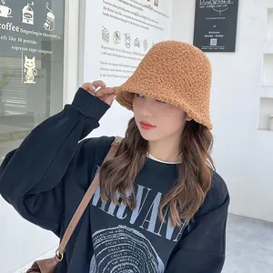 Detail shot of a plush brown sherpa bucket hat worn by a model in a cozy café environment.