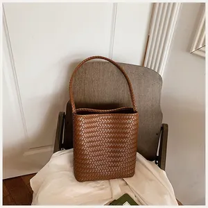 Vista detallada del bolso cubo de cuero trenzado marrón sobre una silla moderna