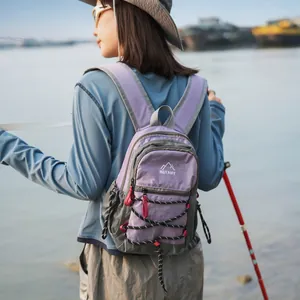 Frau mit leichtem lila Outdoor-Wanderrucksack mit Berg-Logo am Ufer eines Gewässers