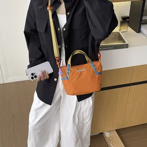 Detail of an orange large capacity nylon crossbody bag worn by a model.