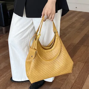 Detailed view of a yellow woven hobo tote bag held by a model in a modern room