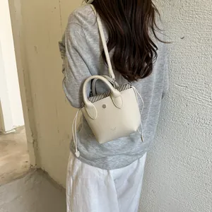 Sac à main seau crème miniature avec doublure à rayures présenté en bandoulière.