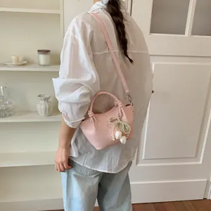 Soft pink crossbody bucket bag with floral bow charm worn over a white linen shirt