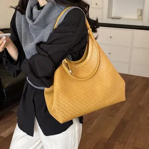 Detailed view of a yellow woven hobo bag carried by a model in a stylish indoor setting.