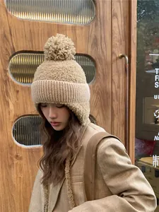 Vrouwelijk model met een beige gebreide muts met pompon en oorkleppen in buitenomgeving
