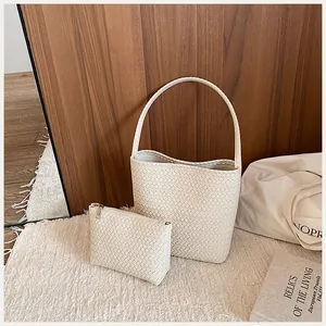 Detalle de un elegante bolso de cubo trenzado beige y neceser a juego en alfombra