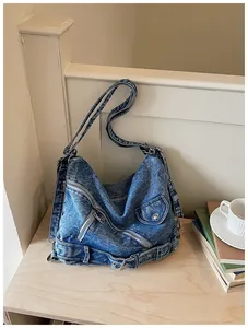 Sac bandoulière en jean vintage avec zips et détails de ceinture sur une table en bois.
