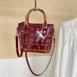 Front view of a dark red patent leather bucket bag featuring a stylish bamboo handle.