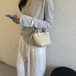Gros plan d'un mini sac seau beige minimaliste avec fermeture à cordon sur modèle
