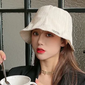 Stylish beige pleated sun bucket hat for women shown in a minimalist cafe setting