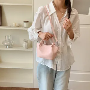 Trendy pink bucket bag with knot handles shown on a model in a casual indoor setting.