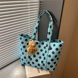 Close-up view of a stylish light blue polka dot tote bag featuring a cute teddy bear charm
