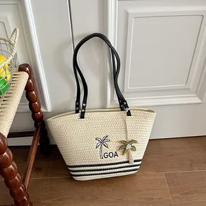 Nahaufnahme einer gewebten Strohtasche mit gestickter Palme und schwarzen Schultergurten.