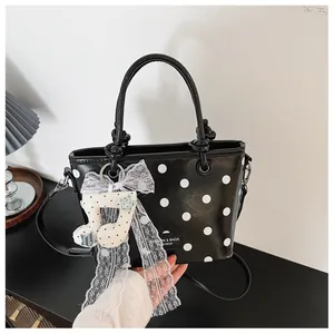 Detail view of a black polka dot handbag featuring a lace bow and musical note charm.