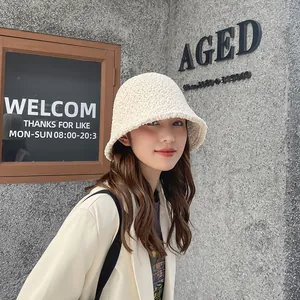 Asian model wearing a cozy beige sherpa bucket hat against a rustic stone wall