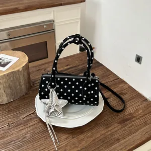 Close-up of a stylish black polka dot cylindrical handbag featuring a silver star charm accessory