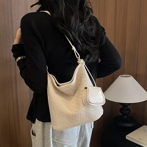 Back view of model carrying a beige woven large capacity bucket bag with mini pouch