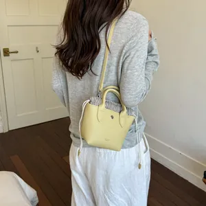 Petit sac seau en cuir jaune minimaliste avec doublure rayée présenté sur un mannequin