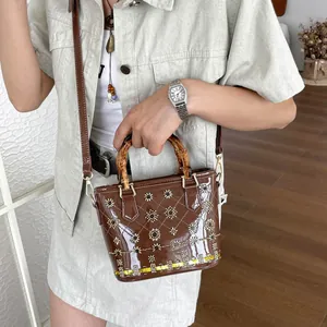 Detailed view of a brown patent leather bucket bag with bamboo handles and floral embroidery