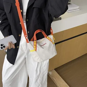 Detailed view of a white striped crossbody bag with vibrant orange straps on a model.