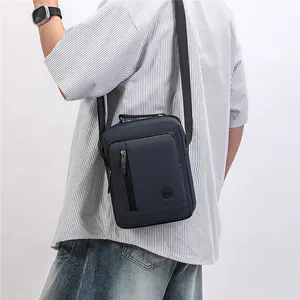 Back view of a casual navy blue crossbody messenger bag worn by a male model in a striped shirt