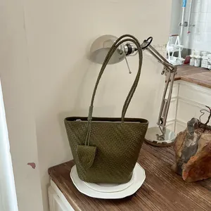 Stijlvolle geweven olijfgroene draagtas met bijpassend zakje op een houten tafel.