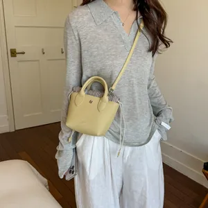 Mini sac seau en cuir jaune porté en bandoulière par un mannequin élégant.