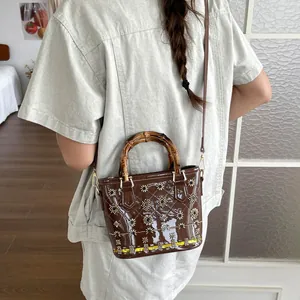 Detail view of a brown patent leather bucket bag with a classic bamboo handle and floral patterns