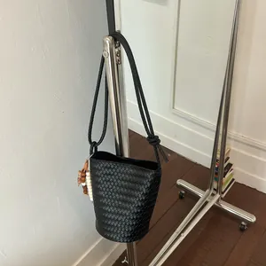 Detailansicht einer schwarzen gewebten Beuteltasche an einem schlichten Metallständer.