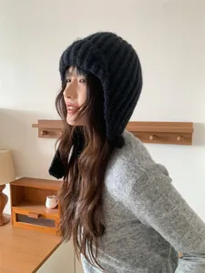 Gemütliche schwarze Strickmütze mit Ohrenklappen an einem Model in einem warmen Raum