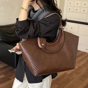 Large brown woven tote bag held by a model in a stylish casual indoor studio setting