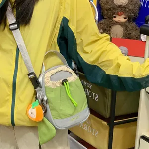 Détail d'un sac de téléphone bandoulière vert avec cordon et breloque orange mignonne