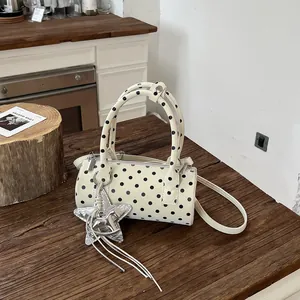 Elegant white polka dot cylinder handbag with silver star charm on a rustic wood surface