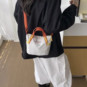 Detail view of a model wearing a stylish off-white crossbody bag with orange straps