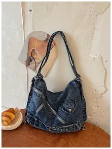 Sac bandoulière en denim vintage avec fermetures éclair et boucles sur une table.