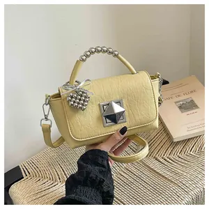 Close-up detail of a chic yellow crossbody bag featuring a beaded handle and pyramid clasp.