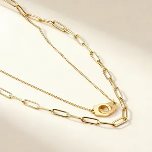 Detail view of double-layer gold necklace featuring handcuff pendant and paperclip chain