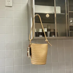 Detail einer beigen geflochtenen Eimertasche mit Perlenanhänger in modernem Ambiente.