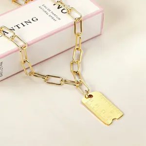 Gros plan détaillé d'un collier pendentif règle créatif en acier inoxydable doré sur boîte.