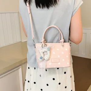 Close-up detail of a pink polka dot crossbody handbag featuring a cute lace musical note charm